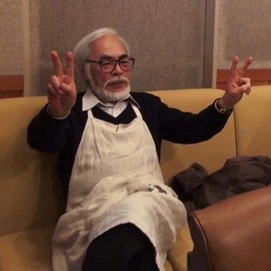 an old man sitting on a couch with his hands in the air and wearing glasses