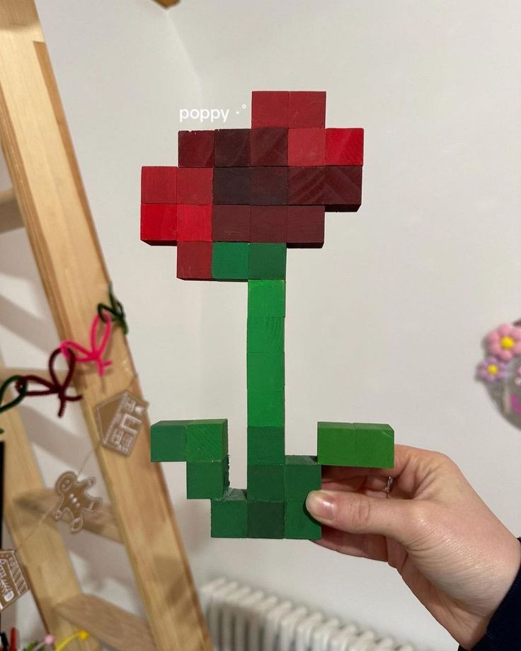 a person holding up a piece of paper made to look like a lego plant with red and green flowers