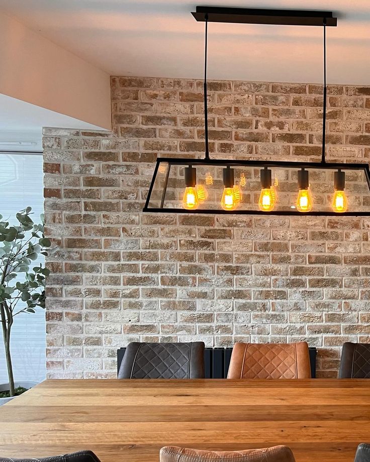 a dining room table and chairs with lights hanging from the ceiling over it in front of a brick wall