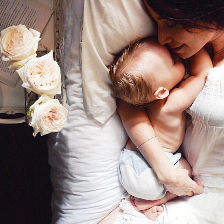 a woman holding a baby in her arms and flowers on the bed next to it