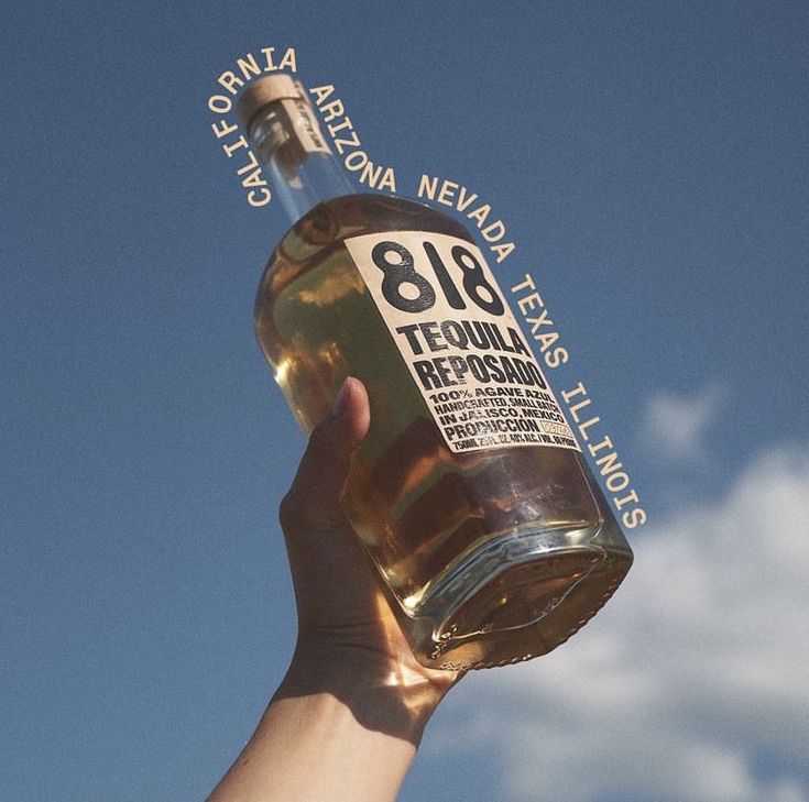 a person holding up a bottle of alcohol in front of a blue sky with white clouds