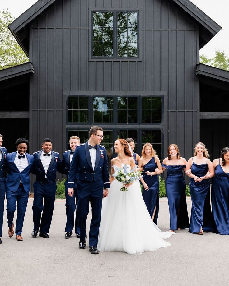 a bride and groom walking with their bridal party in front of a black barn