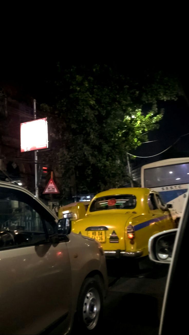 several cars are parked on the side of the road at night, and one is yellow