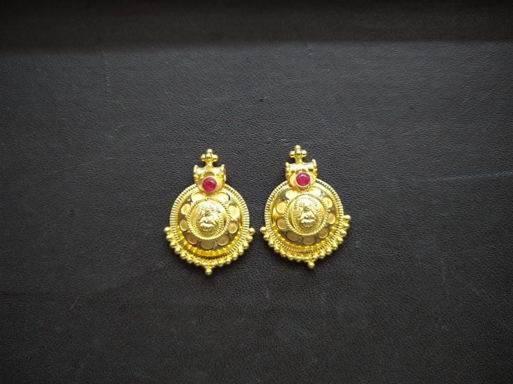 two gold earrings with red stones on them