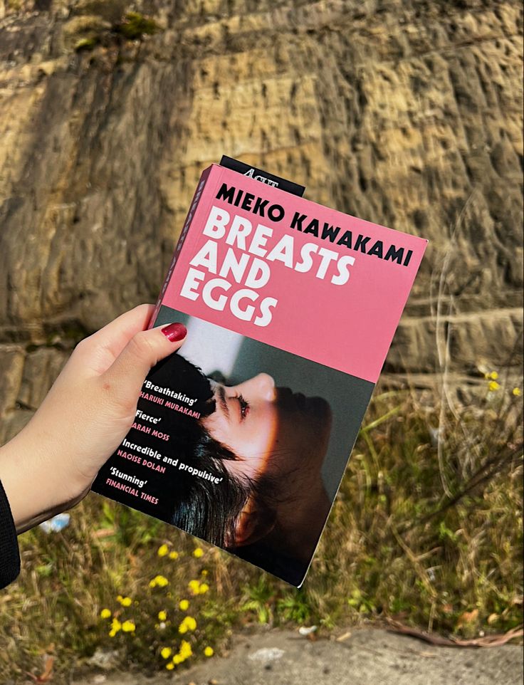 a person holding up a book about breasting and eggs in front of a cliff