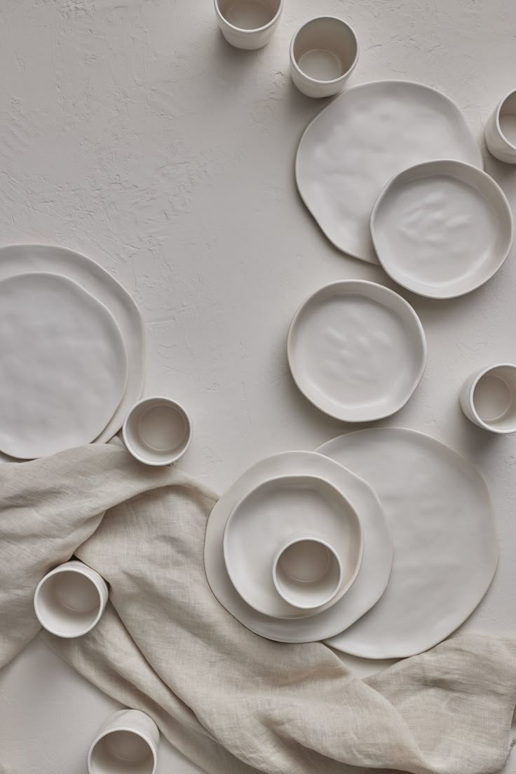 a table topped with lots of white plates and saucers on top of a cloth