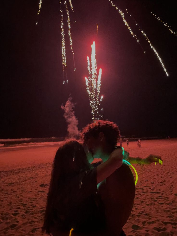 two people kissing on the beach with fireworks in the background