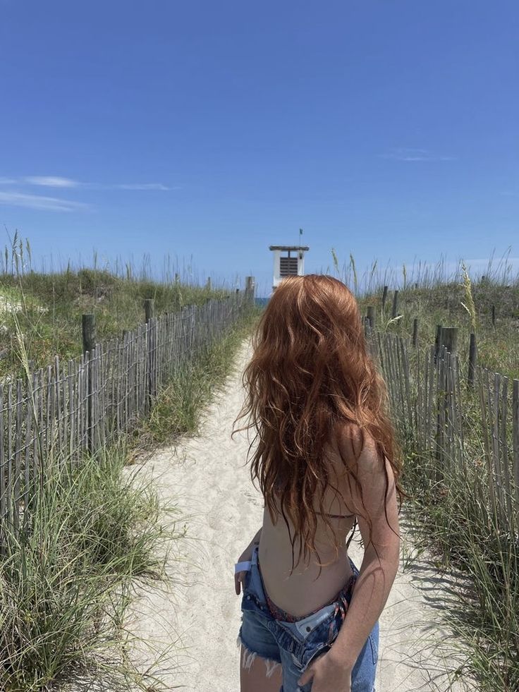 a woman with red hair walking down a sandy path