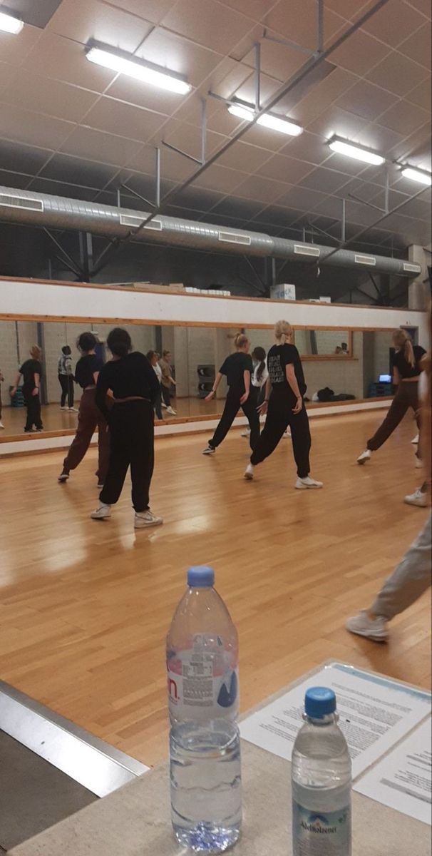 people are dancing in an indoor dance studio with water bottles on the floor and one person is holding a cell phone