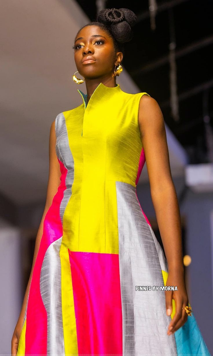 a woman is walking down the runway wearing a colorful dress and headpiece with an earring