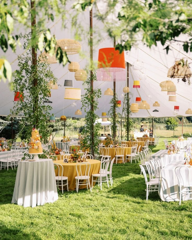 tables and chairs are set up in the grass for an outdoor party with paper lanterns hanging from the ceiling