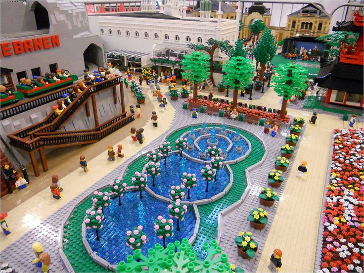 a lego model of a city with people walking around and trees in the middle of it