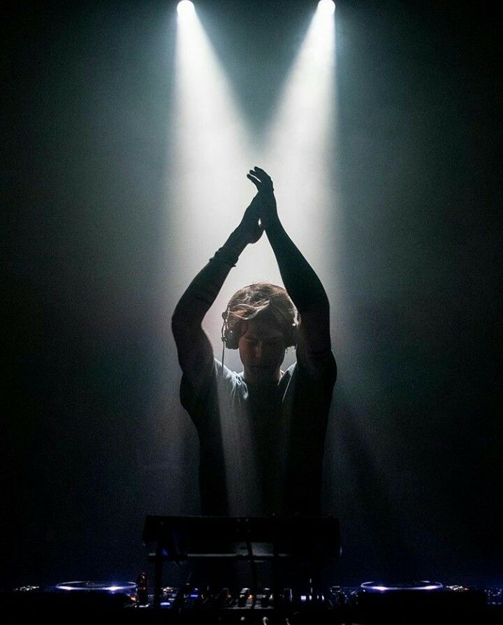 a man standing on top of a stage with his hands in the air and lights behind him