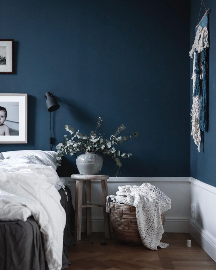 a bedroom with dark blue walls and white bedding is pictured in this image, there are pictures on the wall above the bed