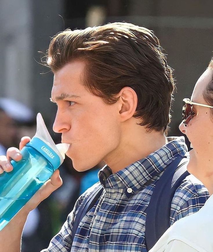 a man drinking from a blue water bottle while standing next to a woman wearing sunglasses