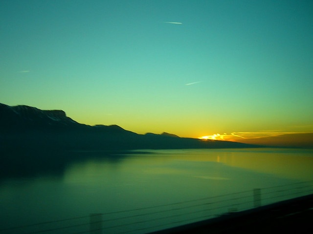 the sun is setting over water and mountains in the distance as seen from a train window