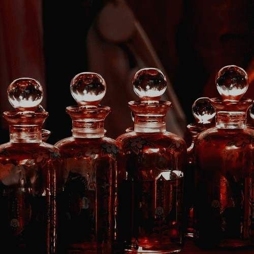 three glass bottles are lined up on a table in front of a red background with the reflection of a woman's face