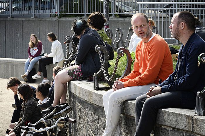 several people sitting on benches with bicycles in front of them and one man looking at the camera