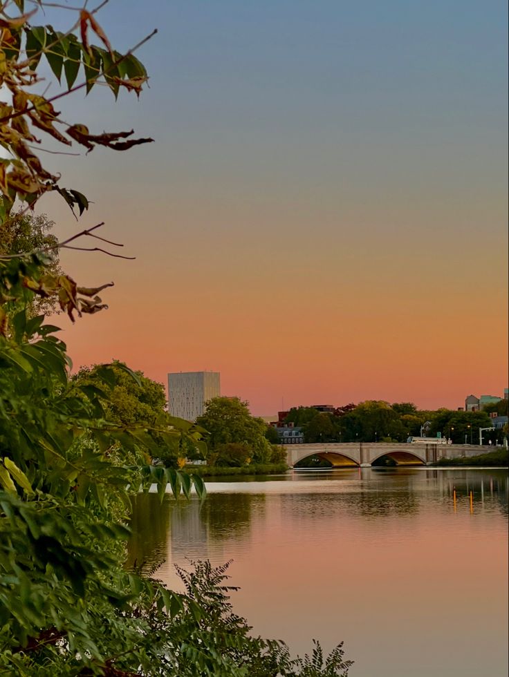 the sun is setting over a lake and bridge