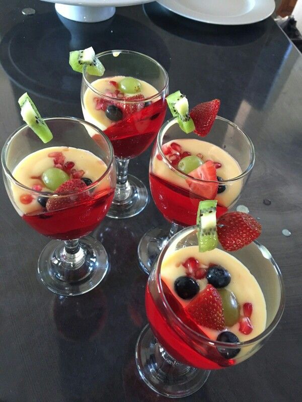 four glasses filled with fruit on top of a black table next to plates and utensils