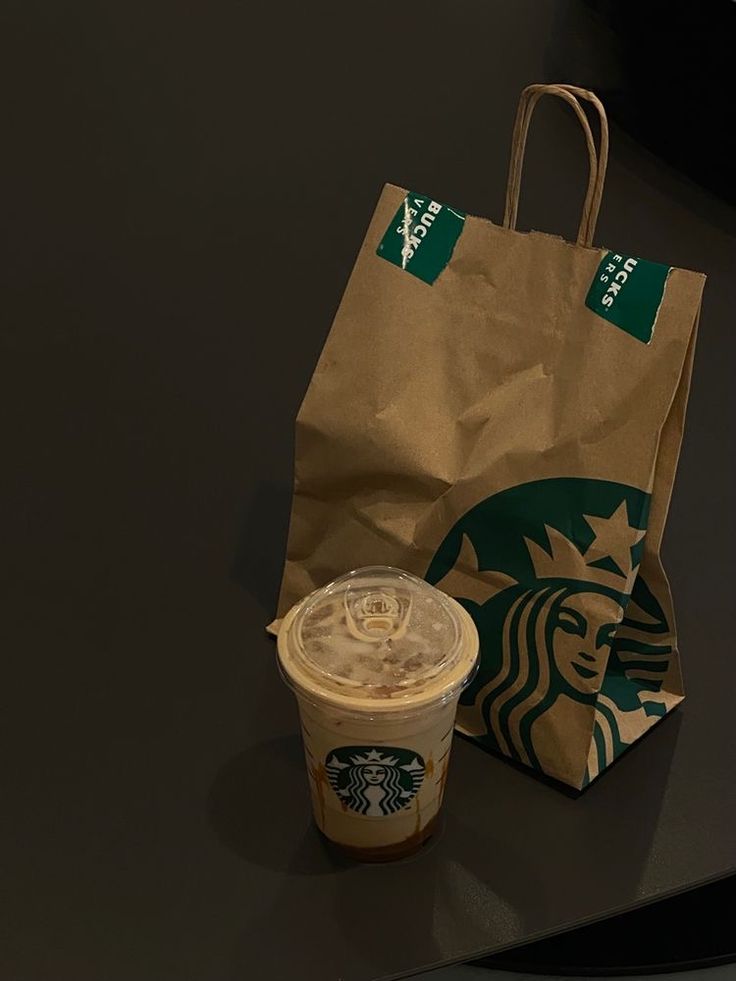 a starbucks coffee cup next to a brown paper bag on a black countertop,