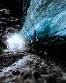 a man standing in an ice cave next to water