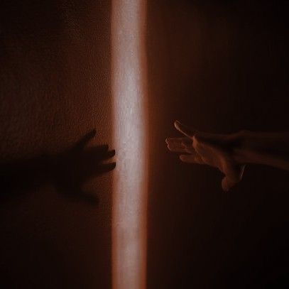 two hands reaching out from behind a wall with light coming through the blinds on it