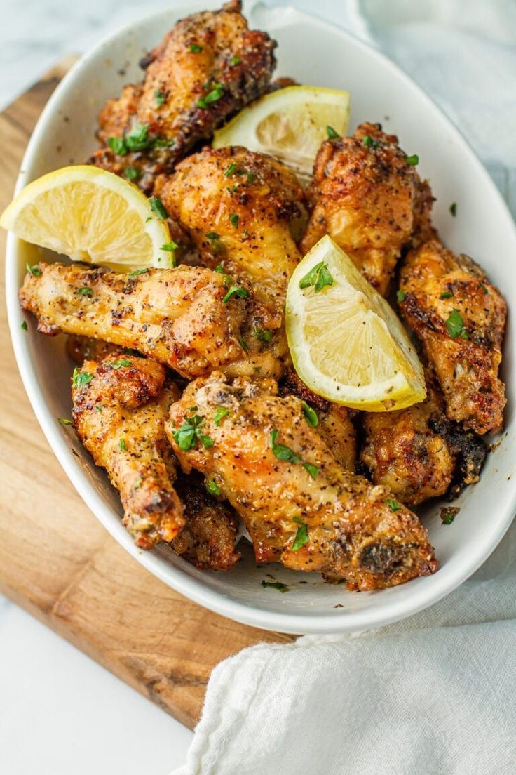 a white bowl filled with chicken wings and lemon wedges