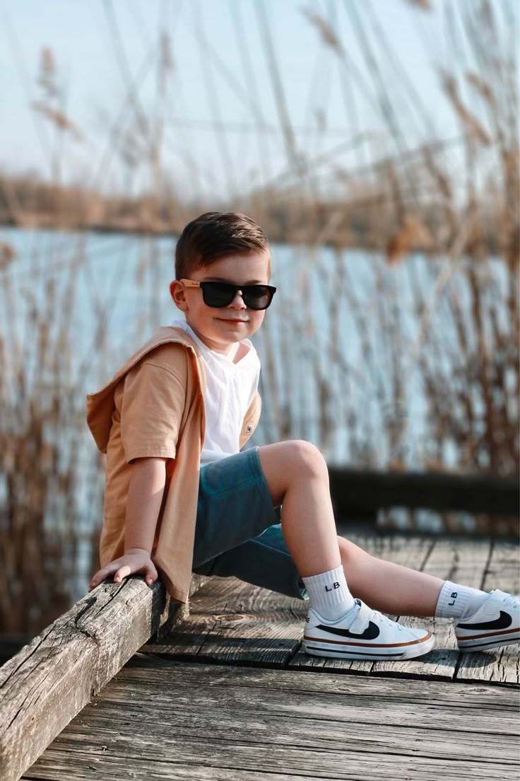 a young boy wearing sunglasses sitting on a dock