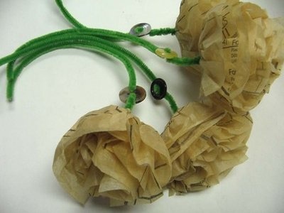 two pieces of brown paper with green string and beads on them sitting on a white surface