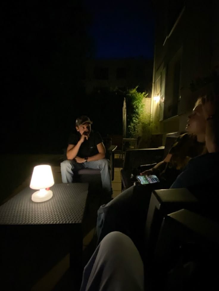 two people sitting on chairs in the dark with one person holding a cell phone to his ear