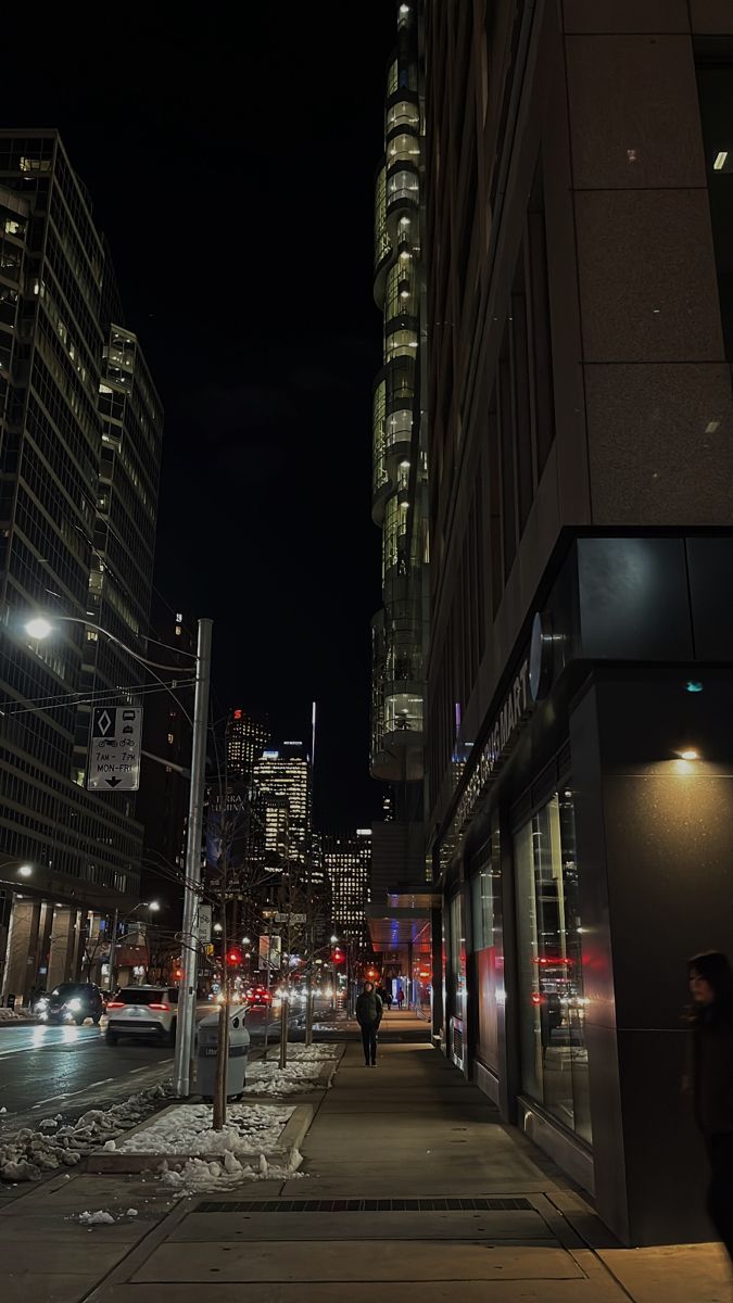 a city street at night with people walking on the sidewalk and buildings in the background