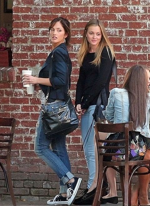 three young women are walking past a brick wall and one is holding a coffee cup