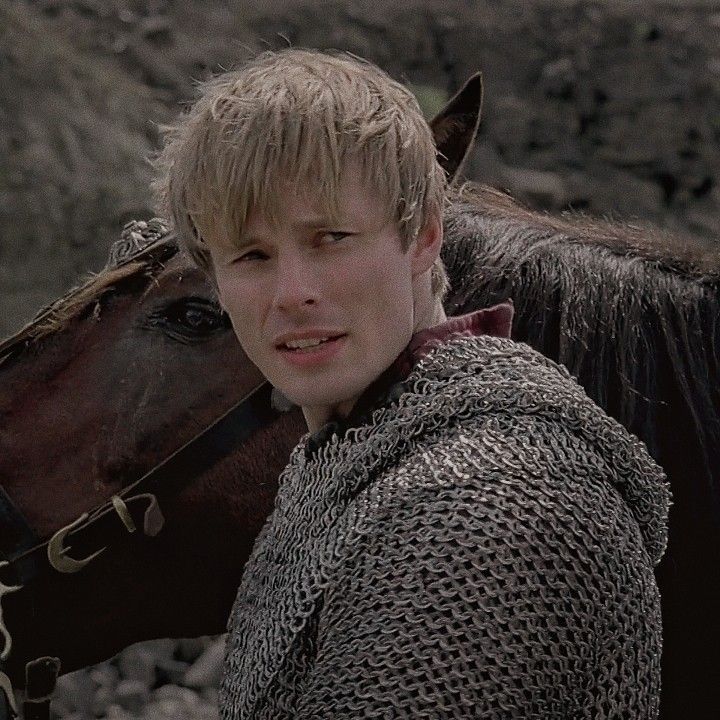 a young man in armor standing next to a horse