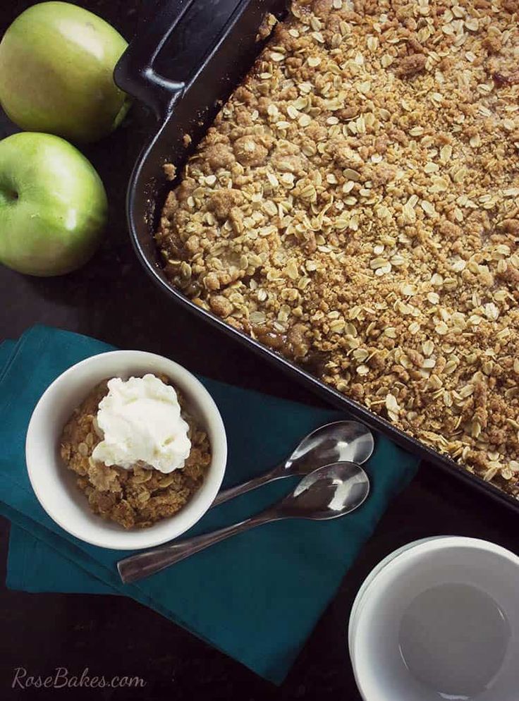 an apple crisp with whipped cream in a bowl and two green apples next to it