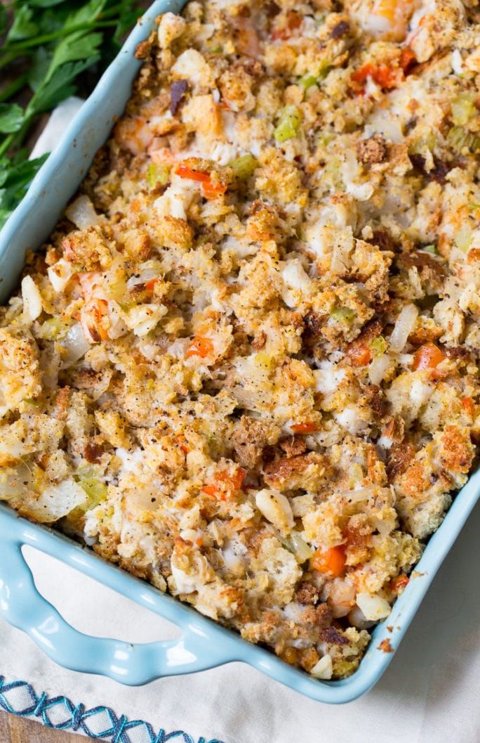 a blue casserole dish filled with stuffing and vegetables on a white table cloth