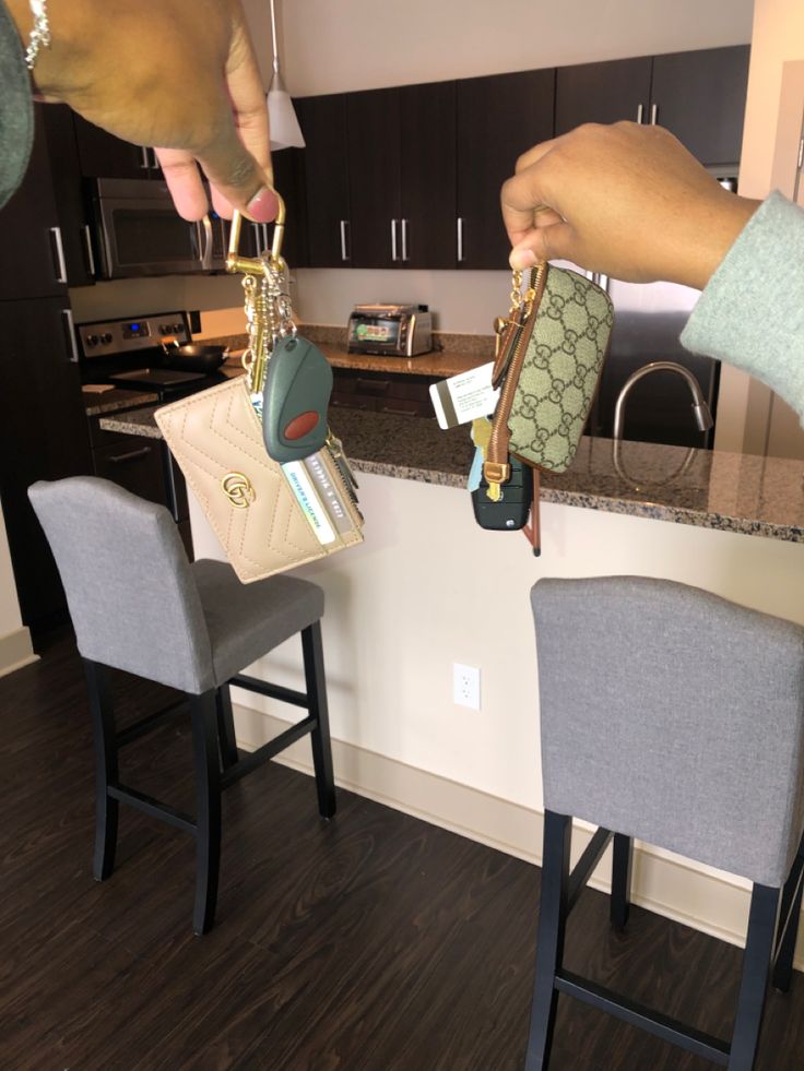 two people holding keys and purses in front of a kitchen counter with bar stools