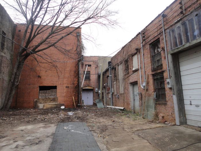 an alley way with old brick buildings and broken down doors on both sides, in the middle of winter