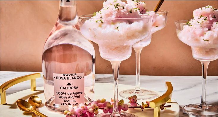 three wine glasses filled with ice cream and pink flowers on a white marble counter top