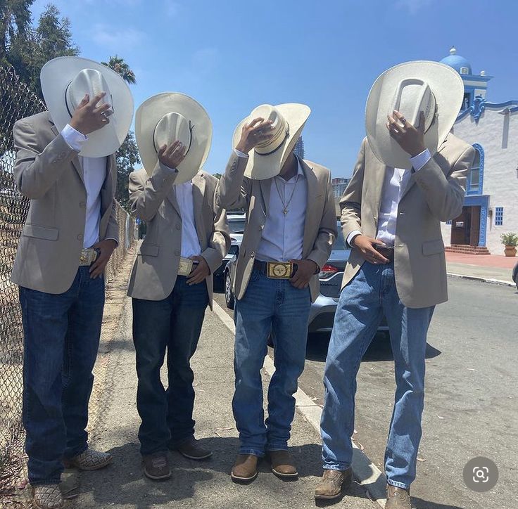 four men in cowboy hats are standing on the side of the road and covering their faces with their hands