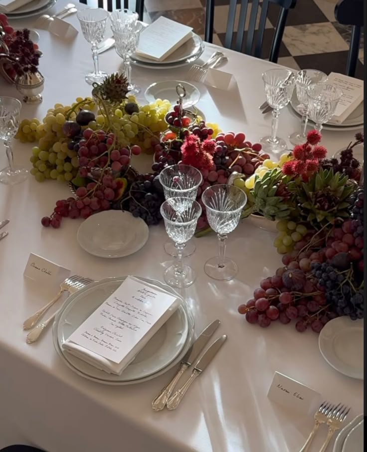 the table is set with plates, silverware and grapes