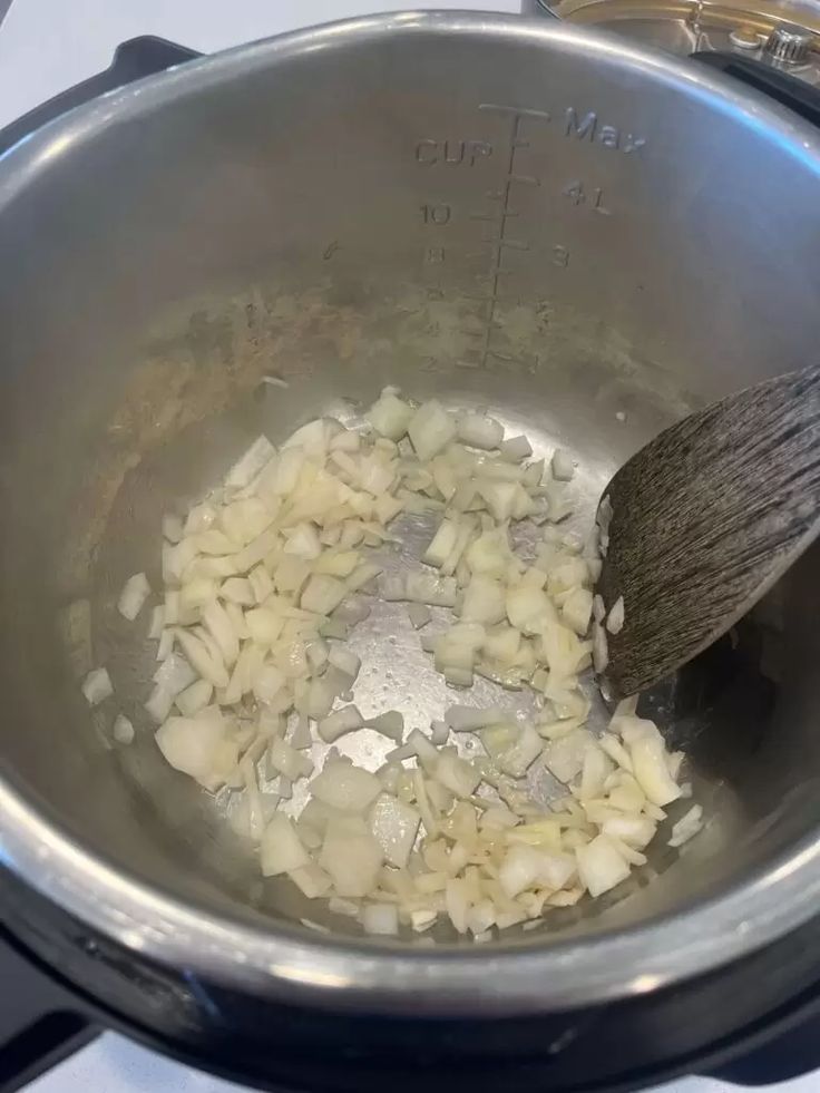 onions being cooked in a pot with a wooden spoon