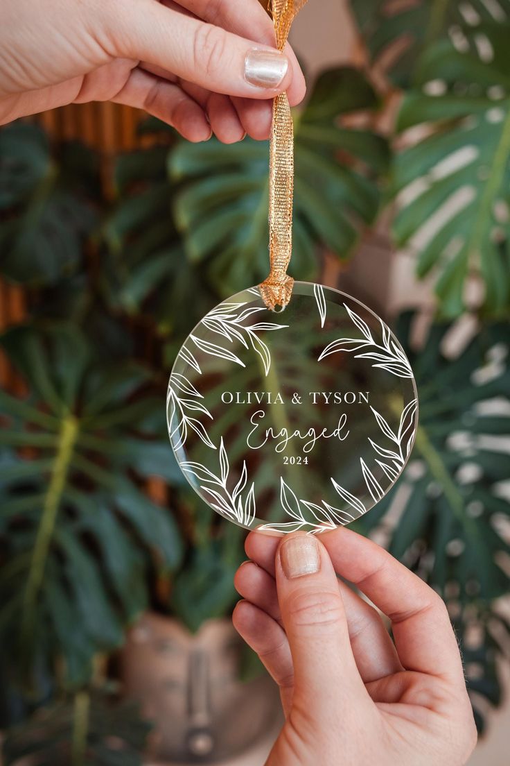 two hands holding a glass ornament with the name of an engaged couple