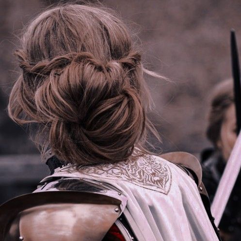 a woman in armor holding two swords and looking at another person with long hair behind her