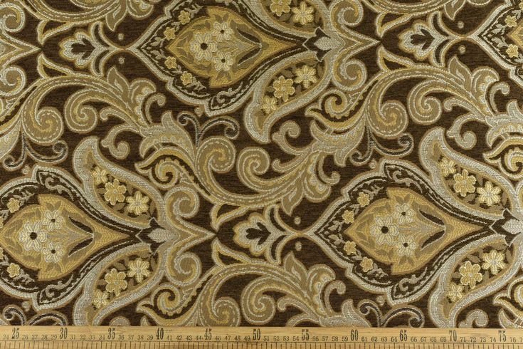 a brown and gold fabric with an ornate design on it's side, next to a ruler