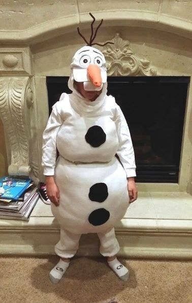 a child dressed as a snowman standing in front of a fire place with books