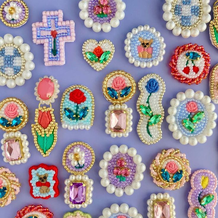 many different types of brooches on a purple surface with pearls and beads around them