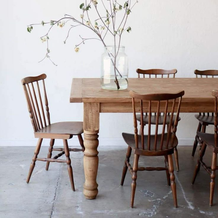 a wooden table with four chairs and a vase filled with flowers sitting on top of it