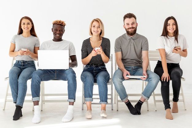 four people sitting on chairs with laptops in front of them and one person holding a cell phone