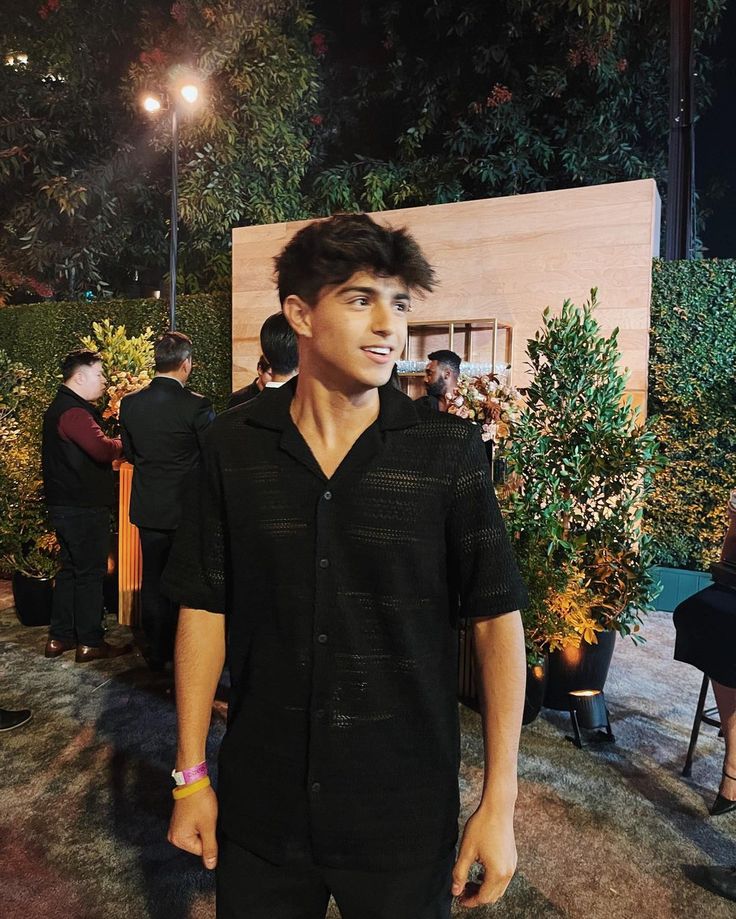 a young man standing in front of a painting at an outdoor event with other people